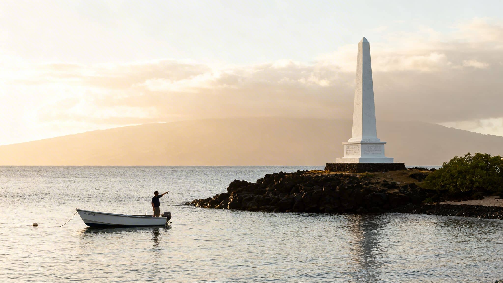 A person in a boat points towards a white obelisk monument on a rocky coast at sunrise.