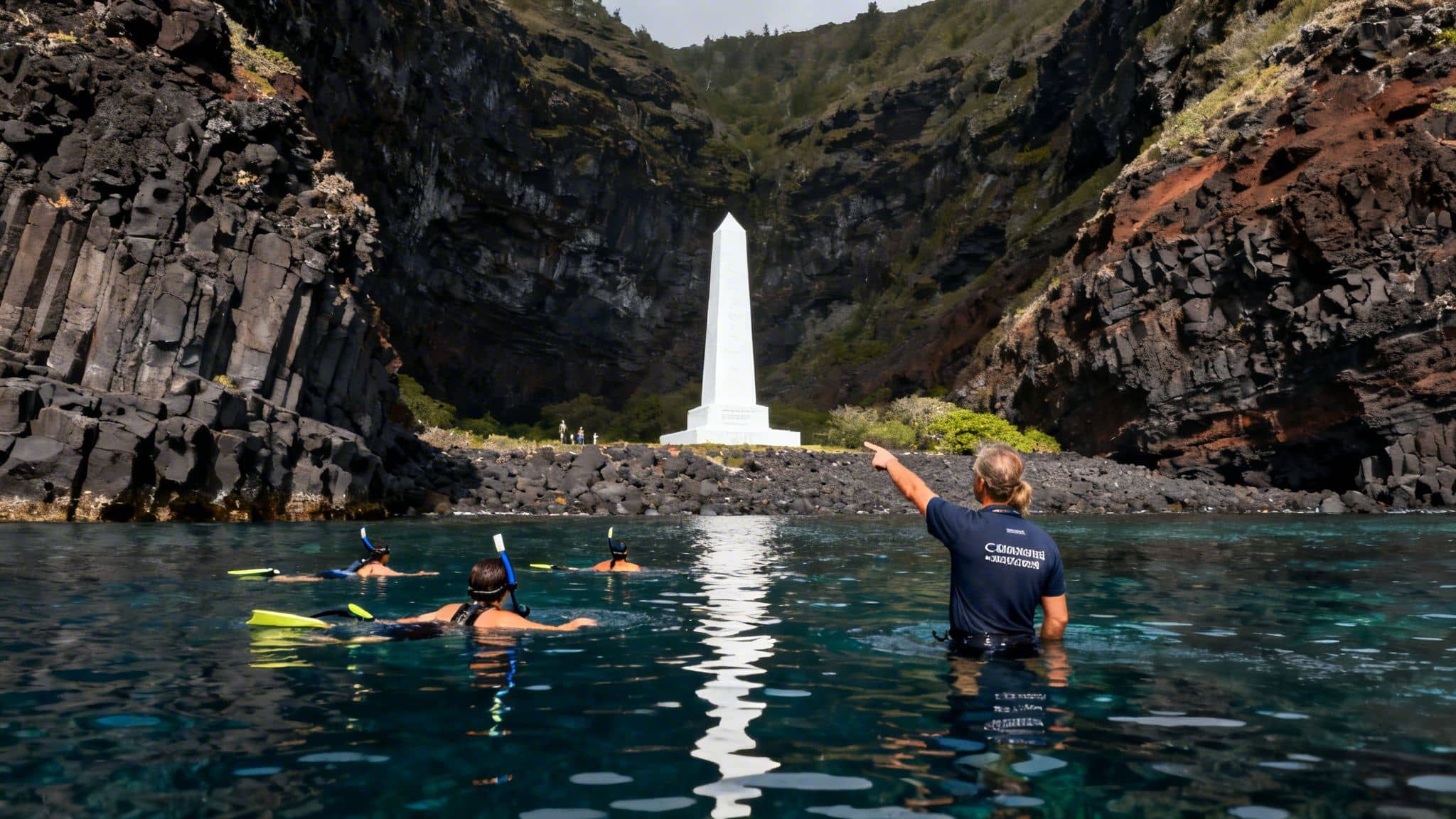 Snorkelers in clear water looking at a white monument on a rocky shore backed by cliffs.