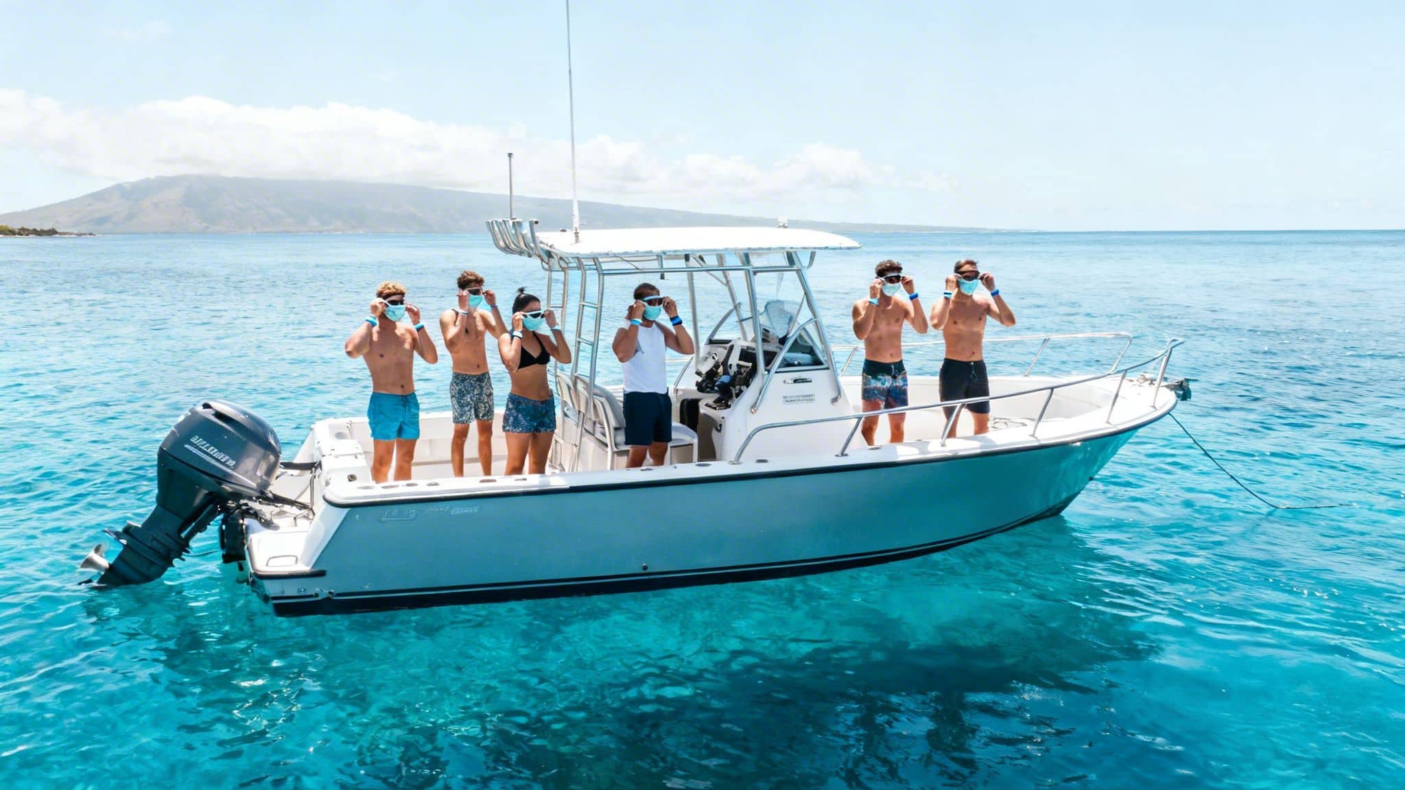 Group of people on a boat in clear ocean water, adjusting goggles and wearing blue wristbands.