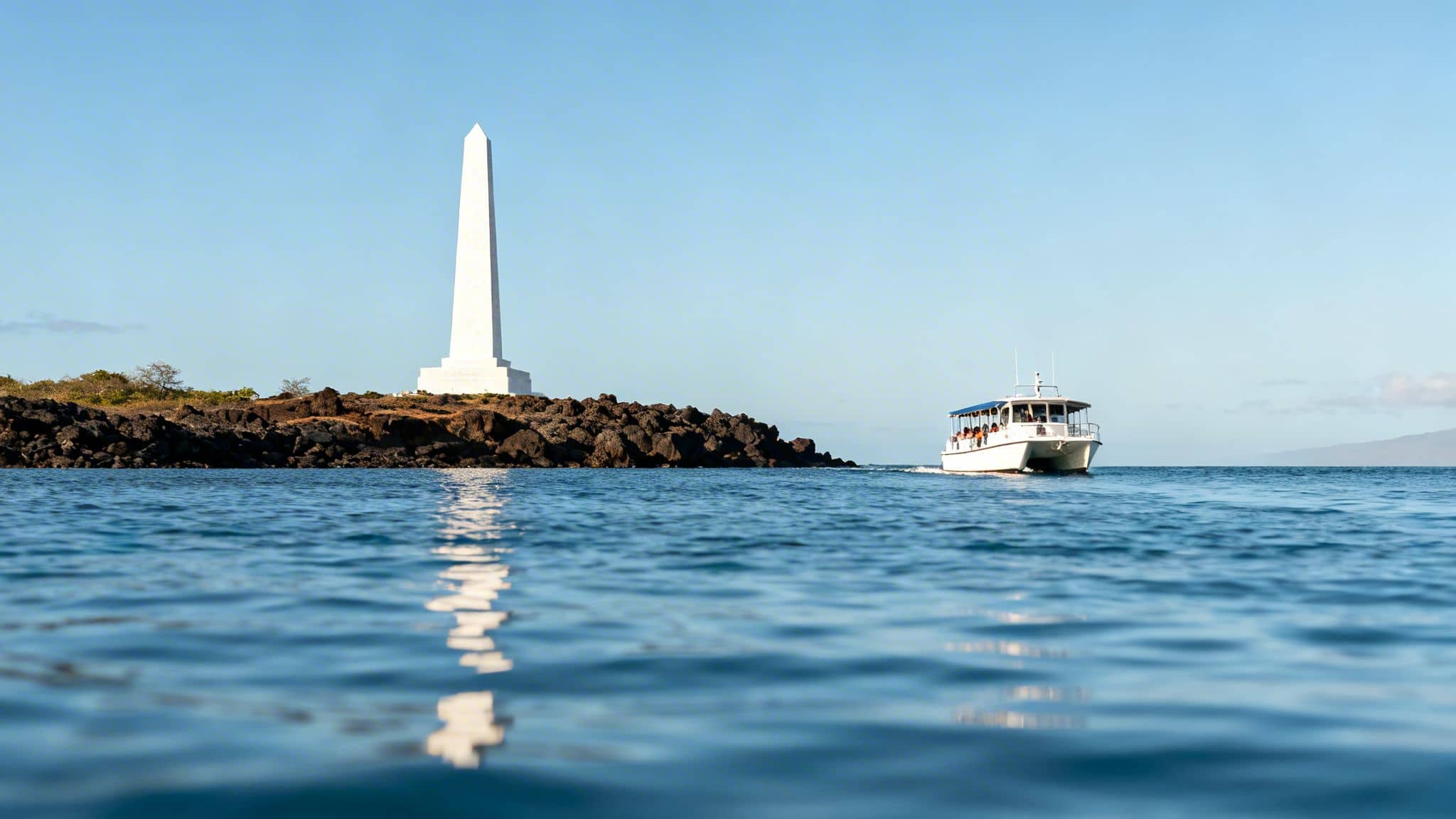 A white obelisk monument on a rocky coast, with a white tour boat on the blue ocean.