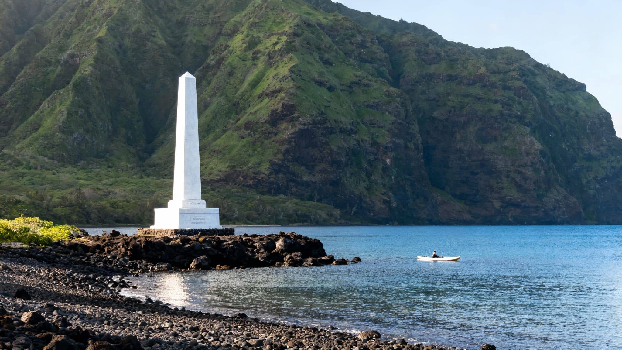Captain Cook monument on a Hawaiian shore with green mountains and a kayaker.