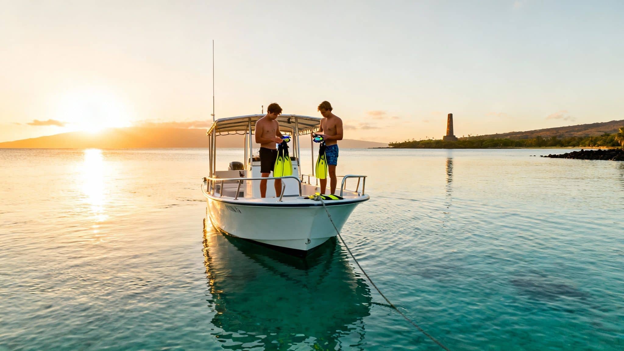 Two men on a boat at sunset preparing to snorkel with fins and masks in clear ocean water.