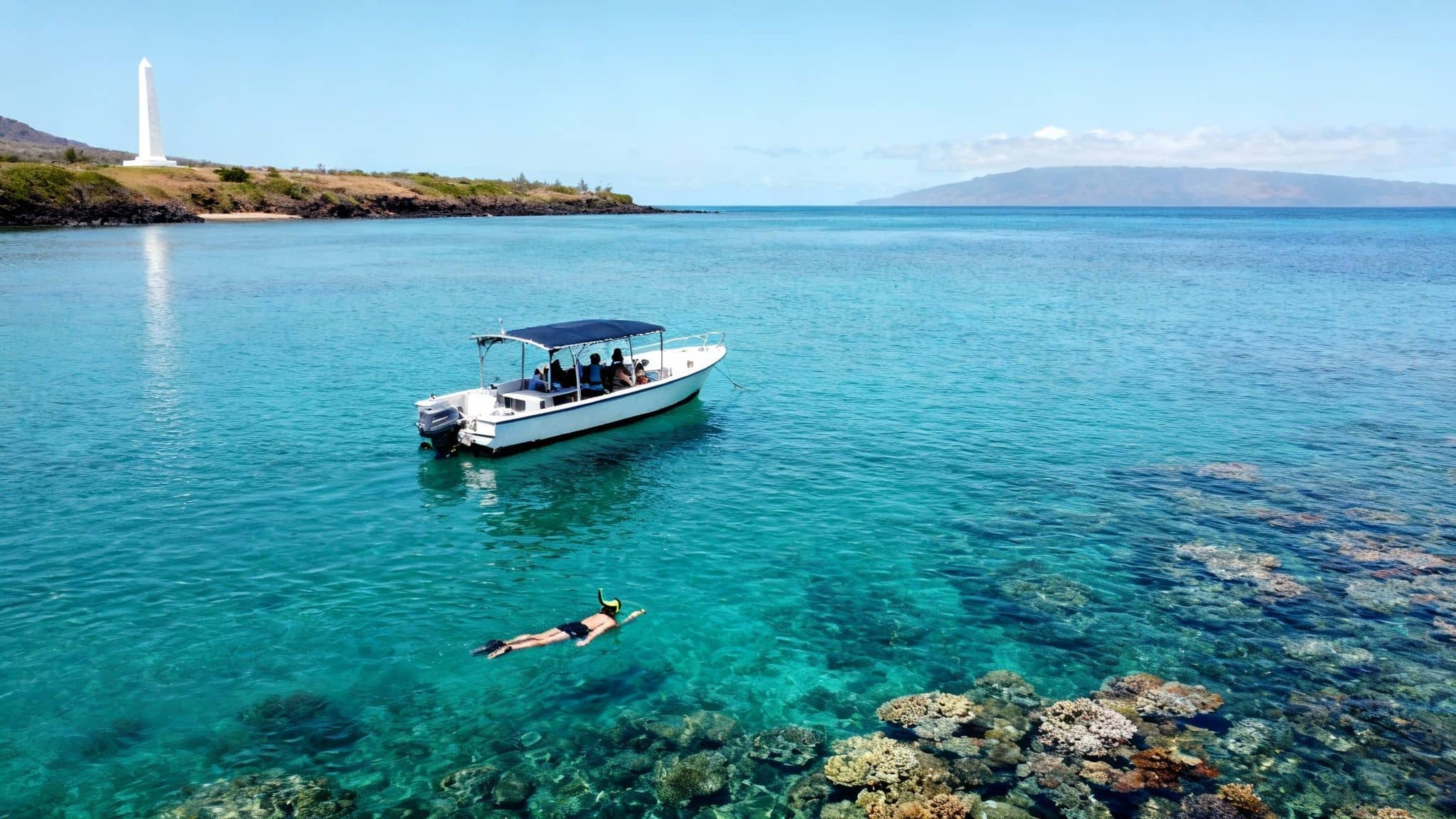 An aerial view of a person snorkeling near a boat over coral reefs, with an obelisk on the shore.