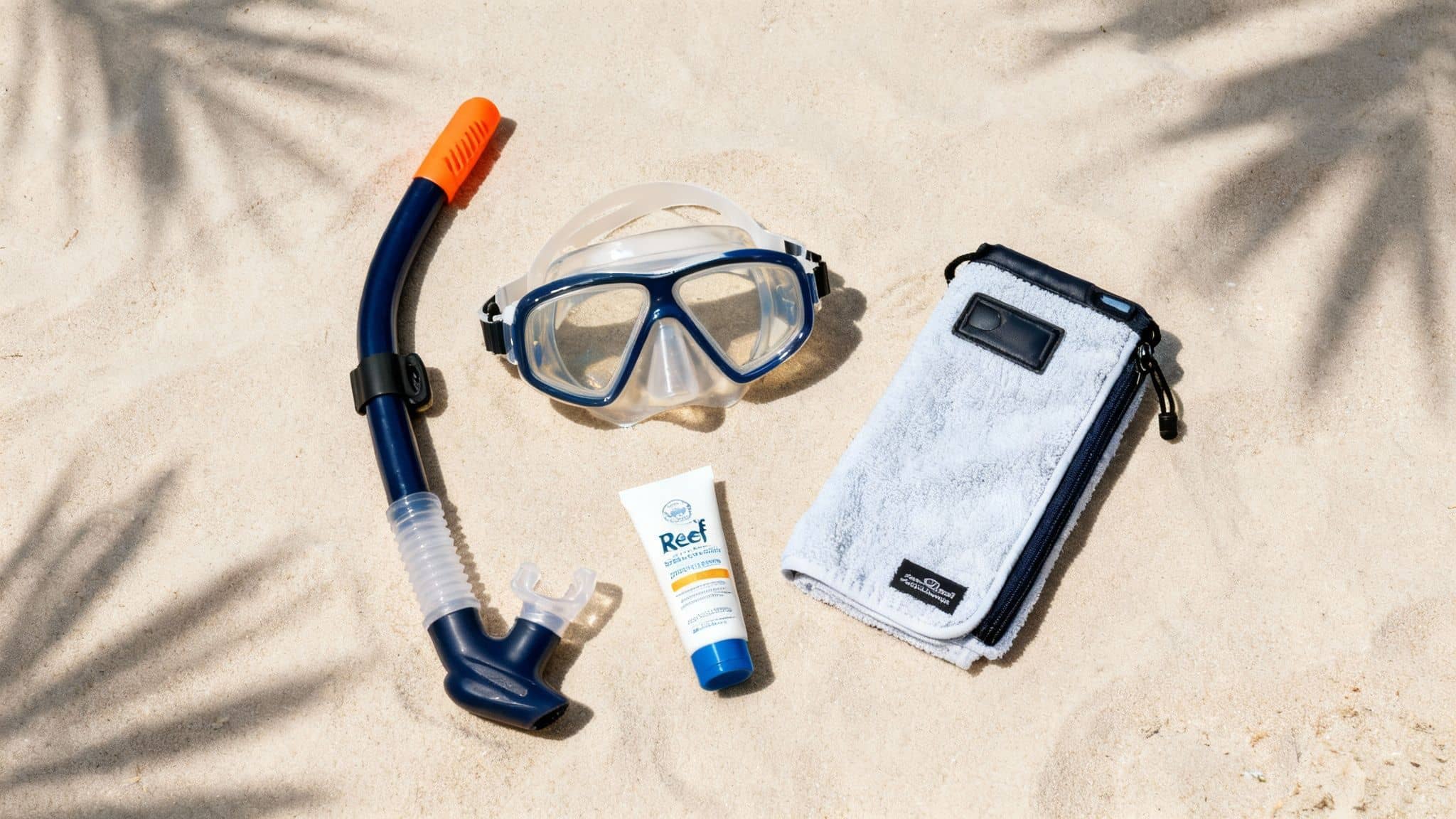 Snorkeling gear including blue mask, snorkel, sunscreen, and waterproof pouch on sandy beach
