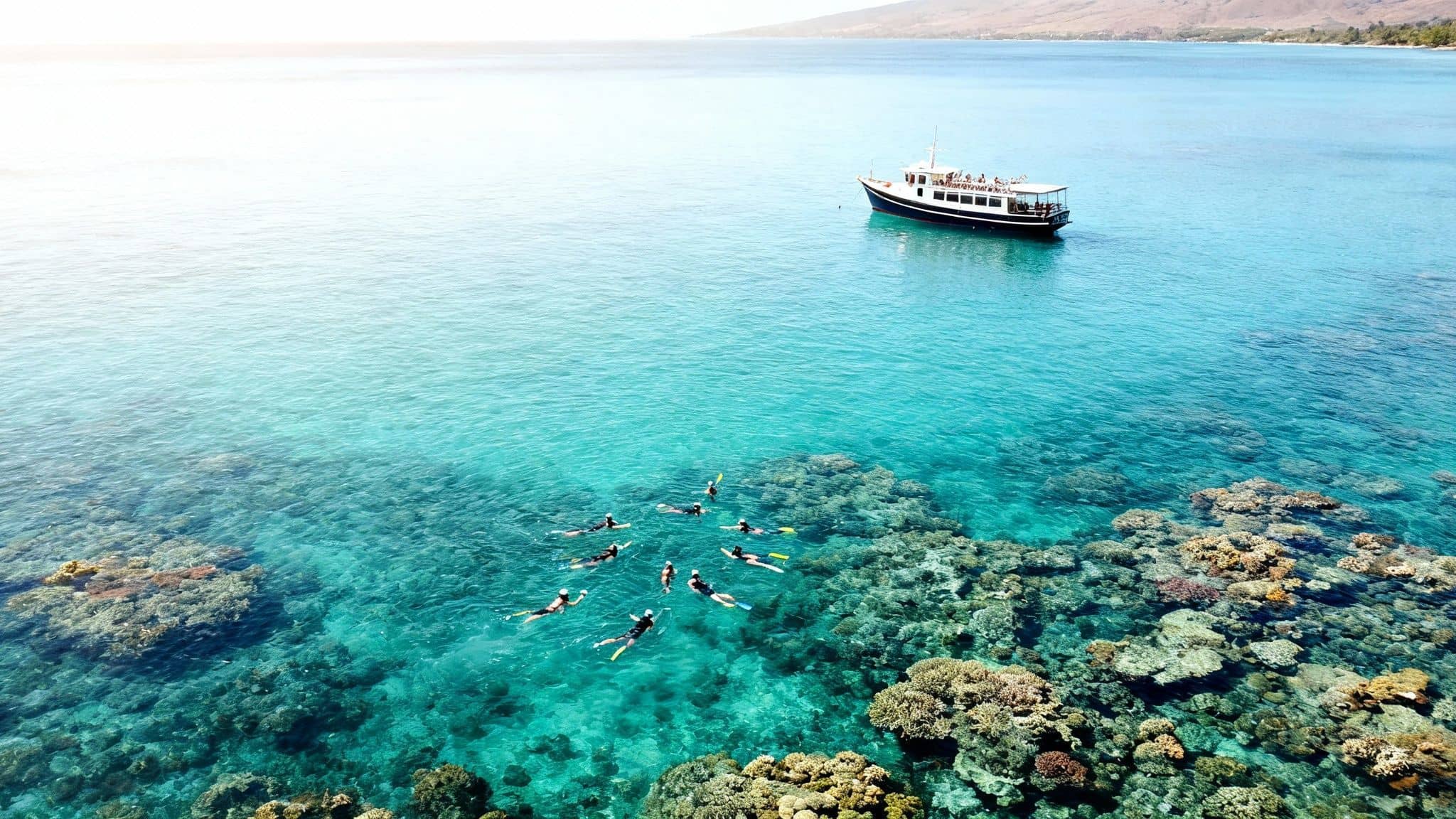 Aerial view of snorkelers and a boat over vibrant coral reefs in clear blue ocean water.