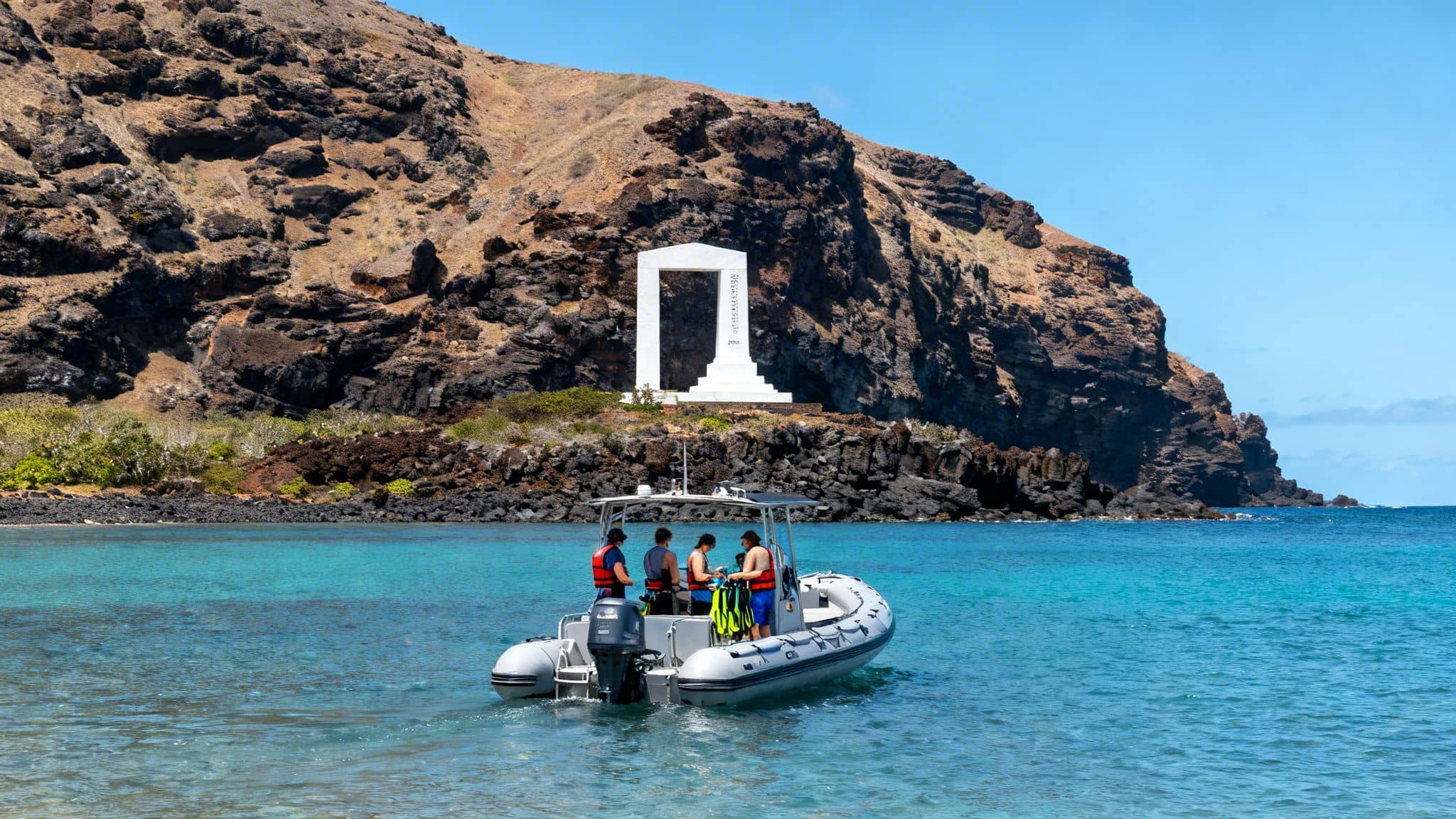 A boat with snorkelers in clear turquoise water near the white Captain Cook monument on a rocky island shore.