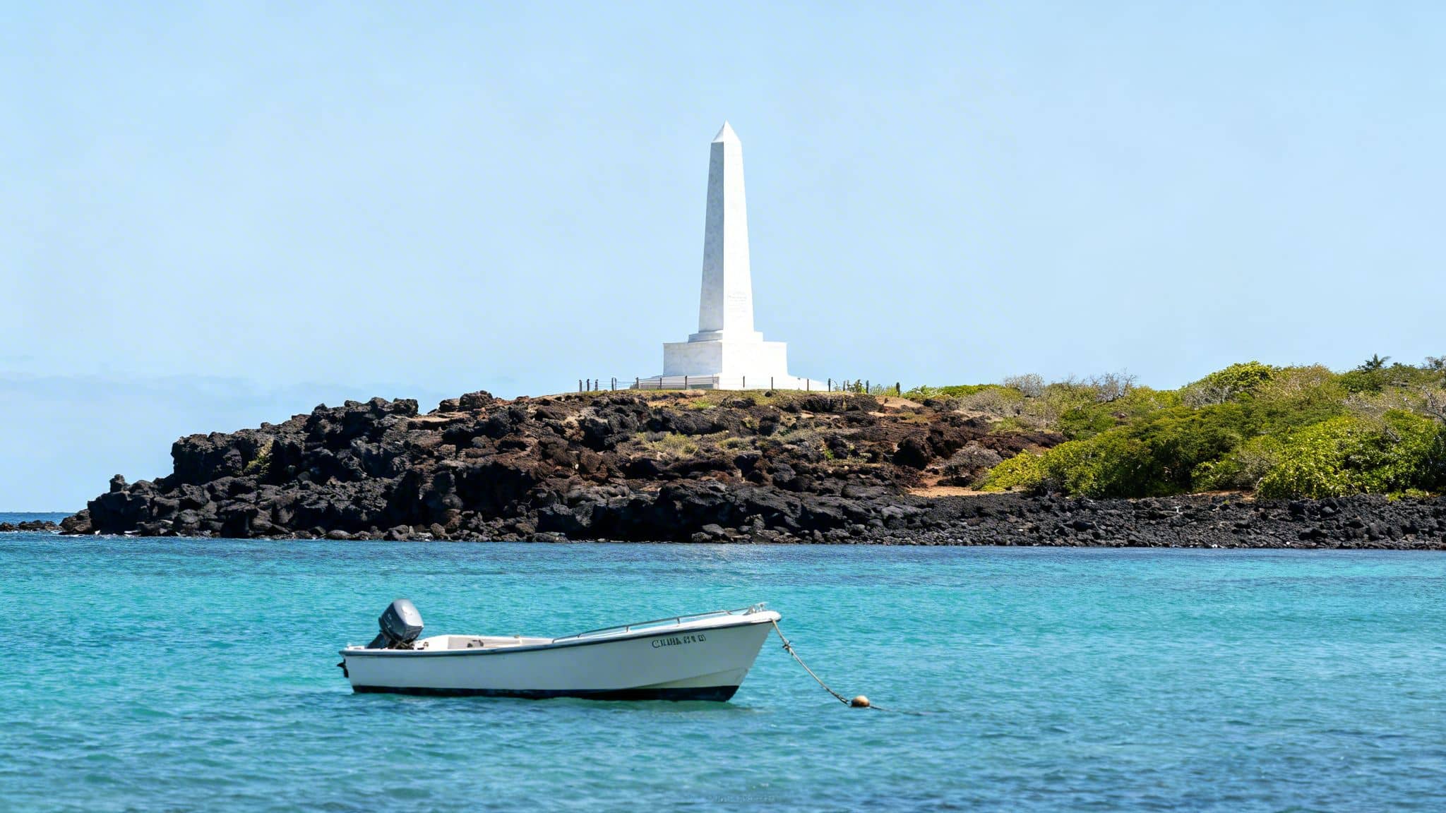 A small white boat floats on clear blue water with a historic white monument on a rocky island.