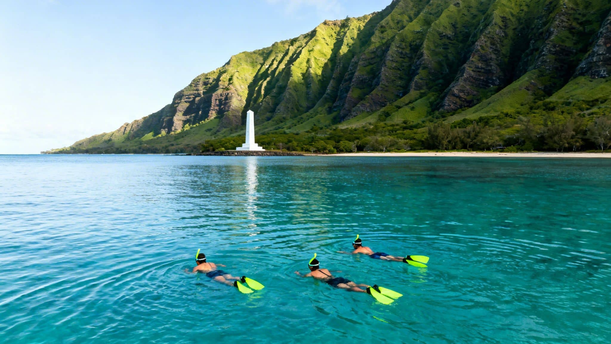 Three people snorkeling in vibrant turquoise waters with a white monument and lush green mountains in Hawaii.