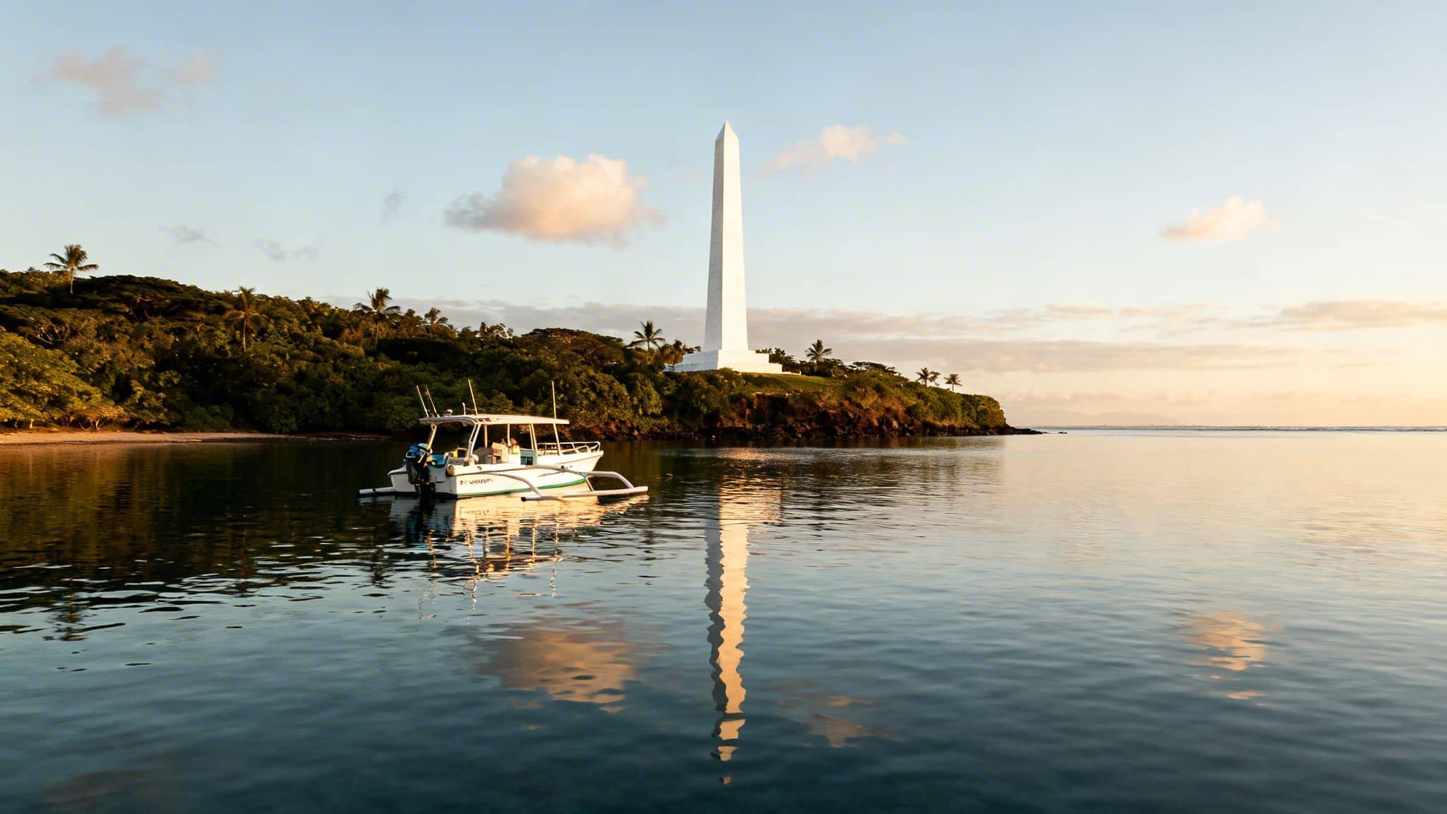 A boat floats on tranquil waters with a tall white obelisk monument on a tropical island.