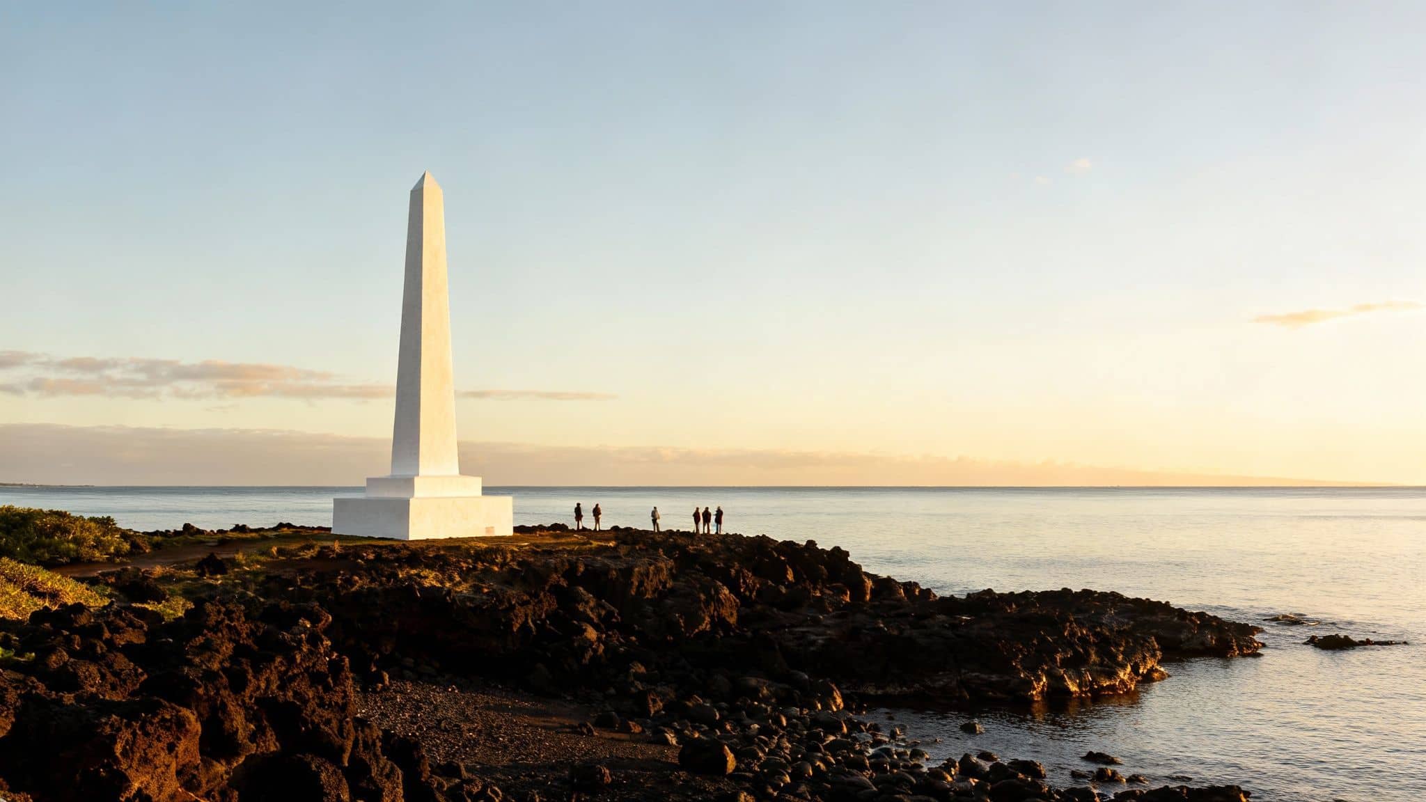 White obelisk monument standing on rocky coastline at sunset with tourists viewing ocean