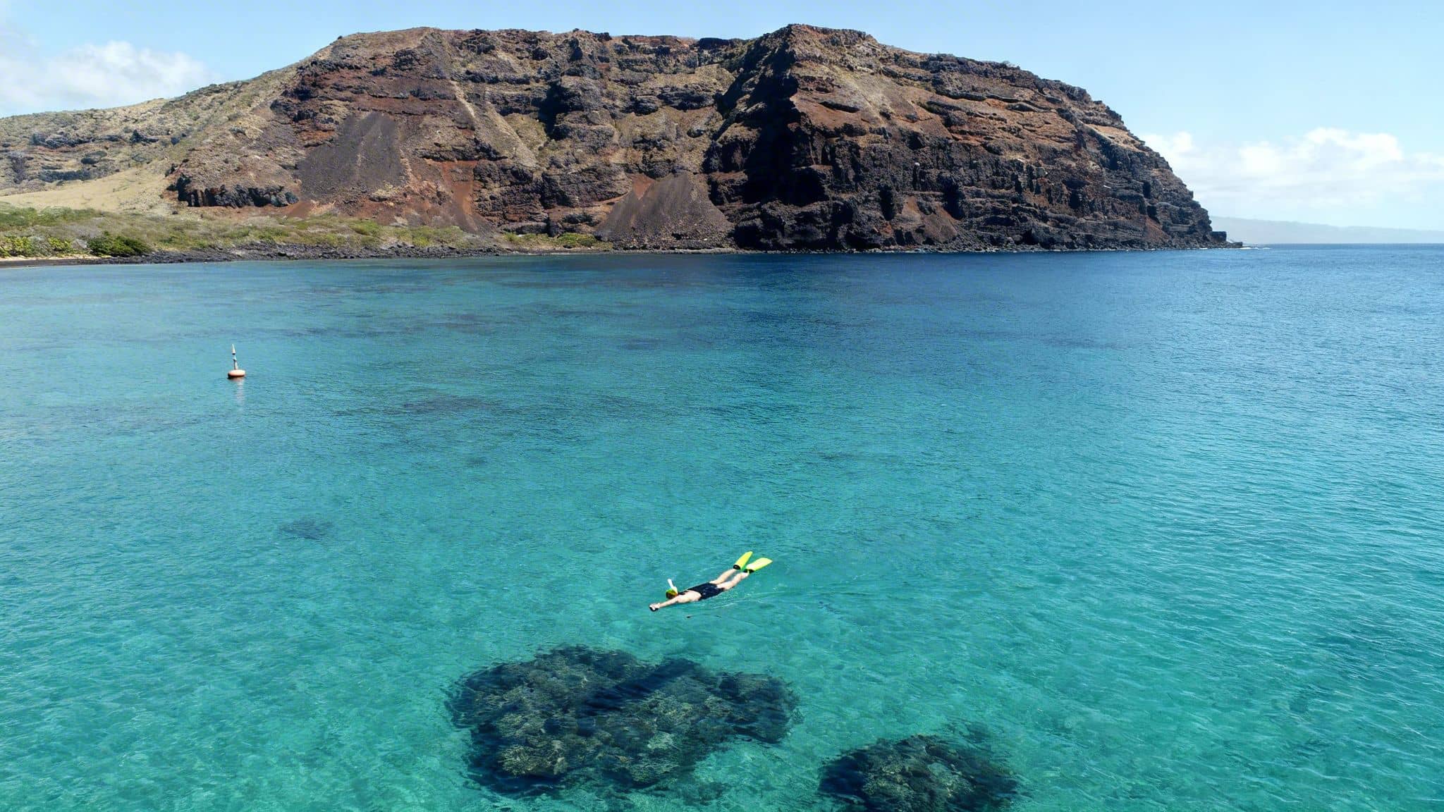 A person swims with a snorkel and fins in clear tropical water next to a rugged island.