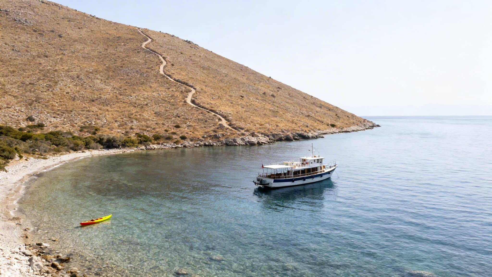Aerial view of a boat and kayak in a clear bay, with a winding path up a dry hill.