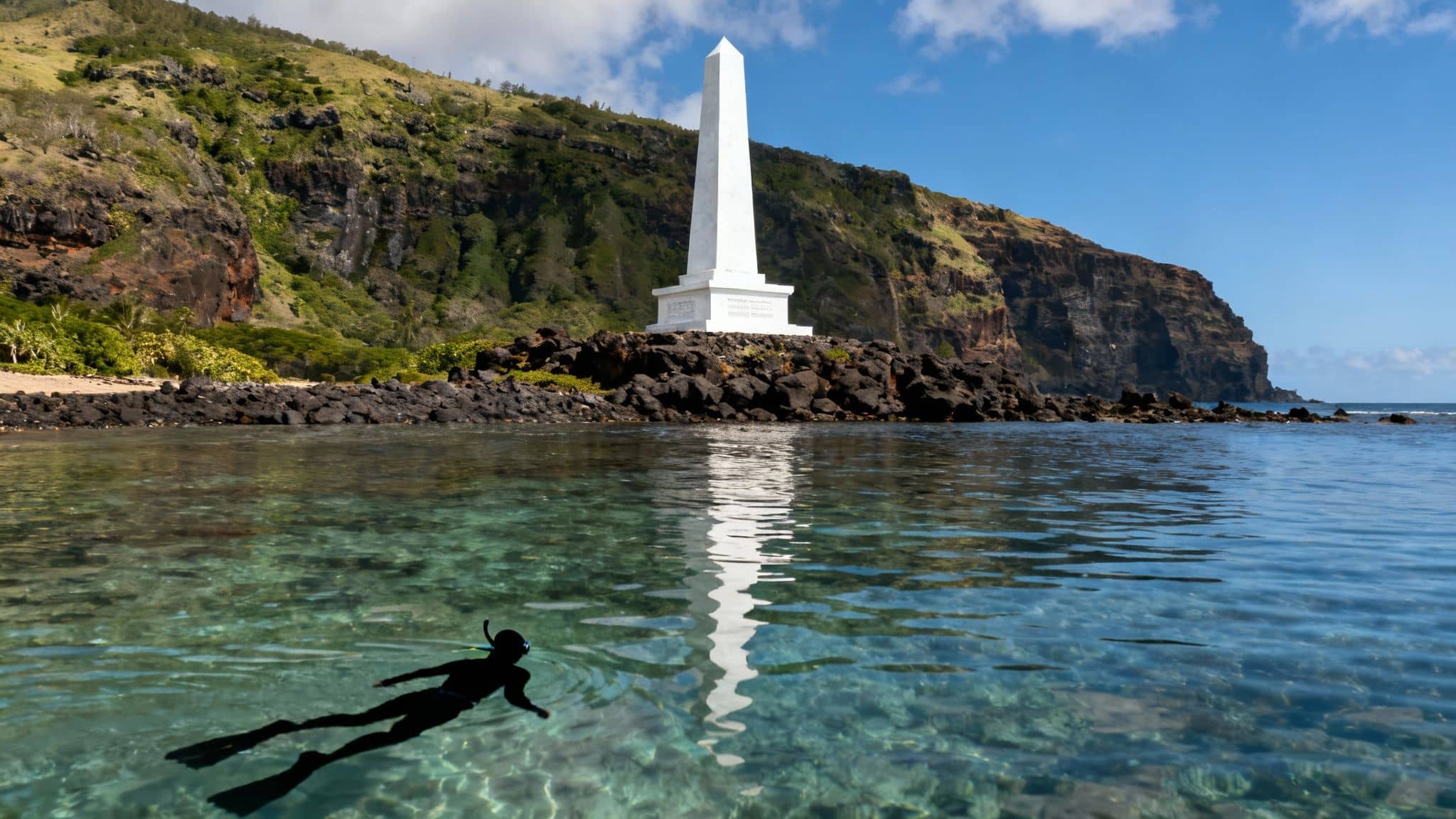 A person snorkeling in clear turquoise water near the Captain Cook monument, surrounded by lush cliffs.