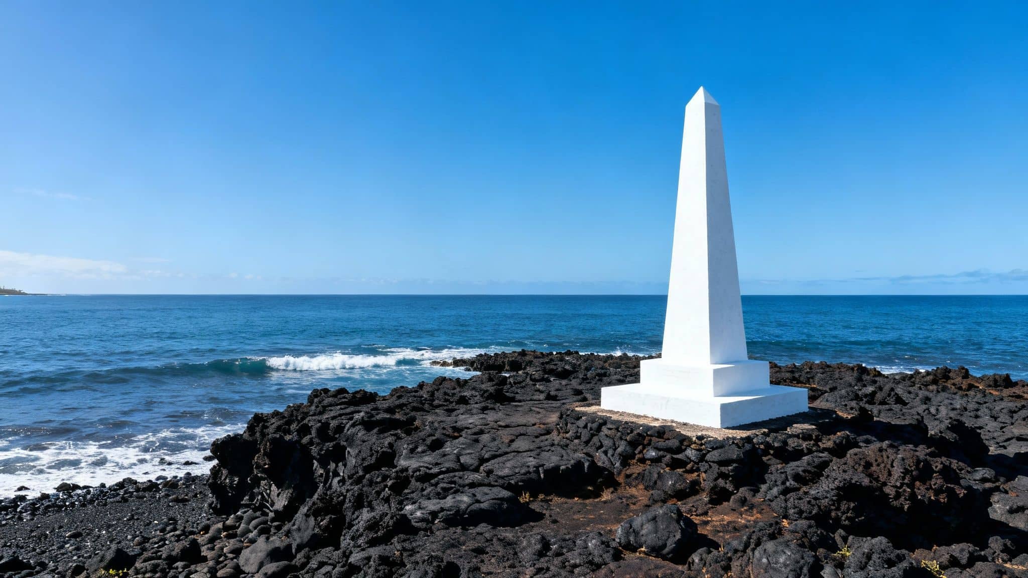 White obelisk monument on black volcanic rocks by the blue Pacific Ocean under a clear sky.