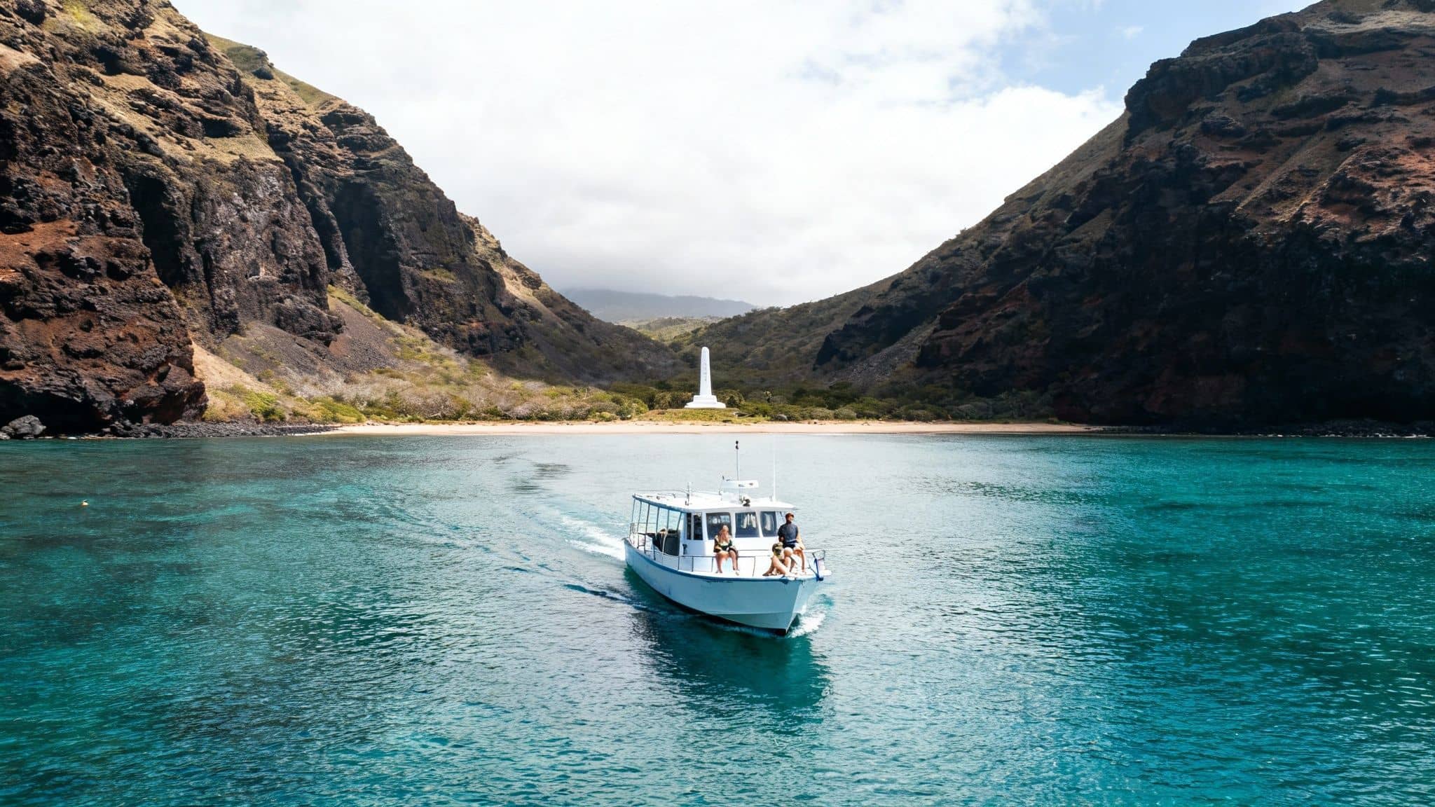 A tour boat with passengers sails in vibrant turquoise water towards a scenic bay with a white monument and towering cliffs.