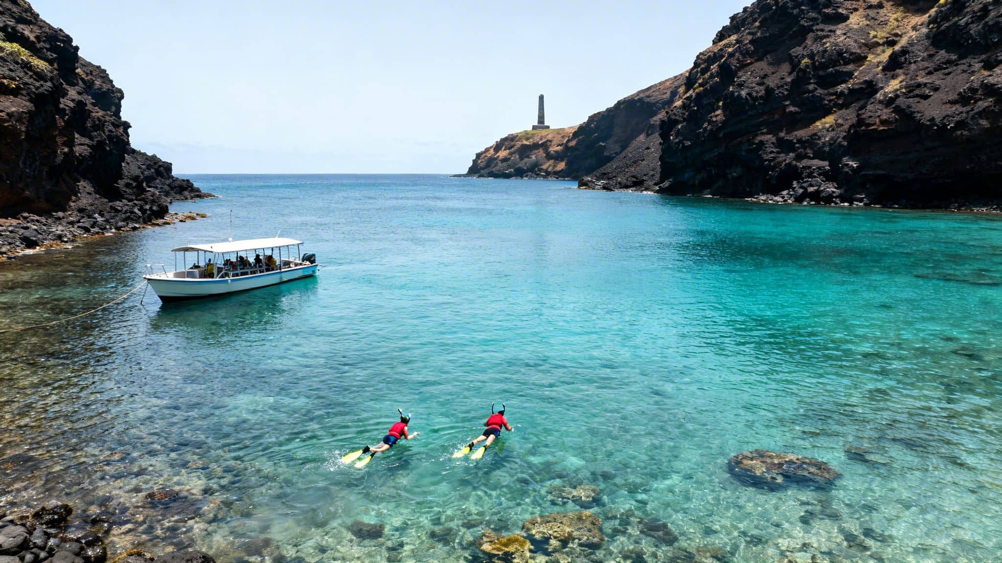 Two people snorkel in clear turquoise waters near a boat, surrounded by rocky cliffs and a distant lighthouse.