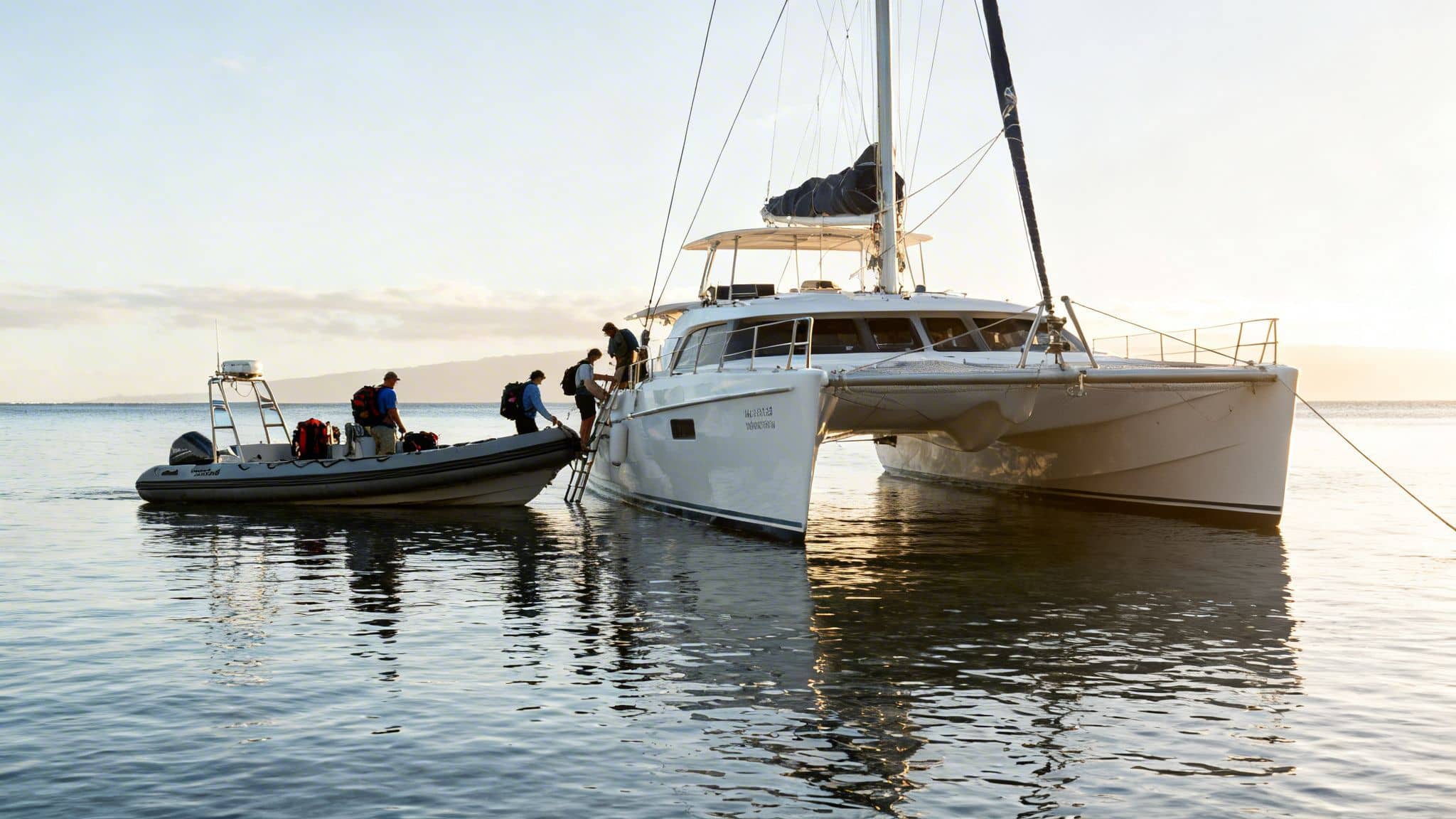 People transfer with backpacks from a rigid inflatable boat to a white catamaran yacht on calm water.