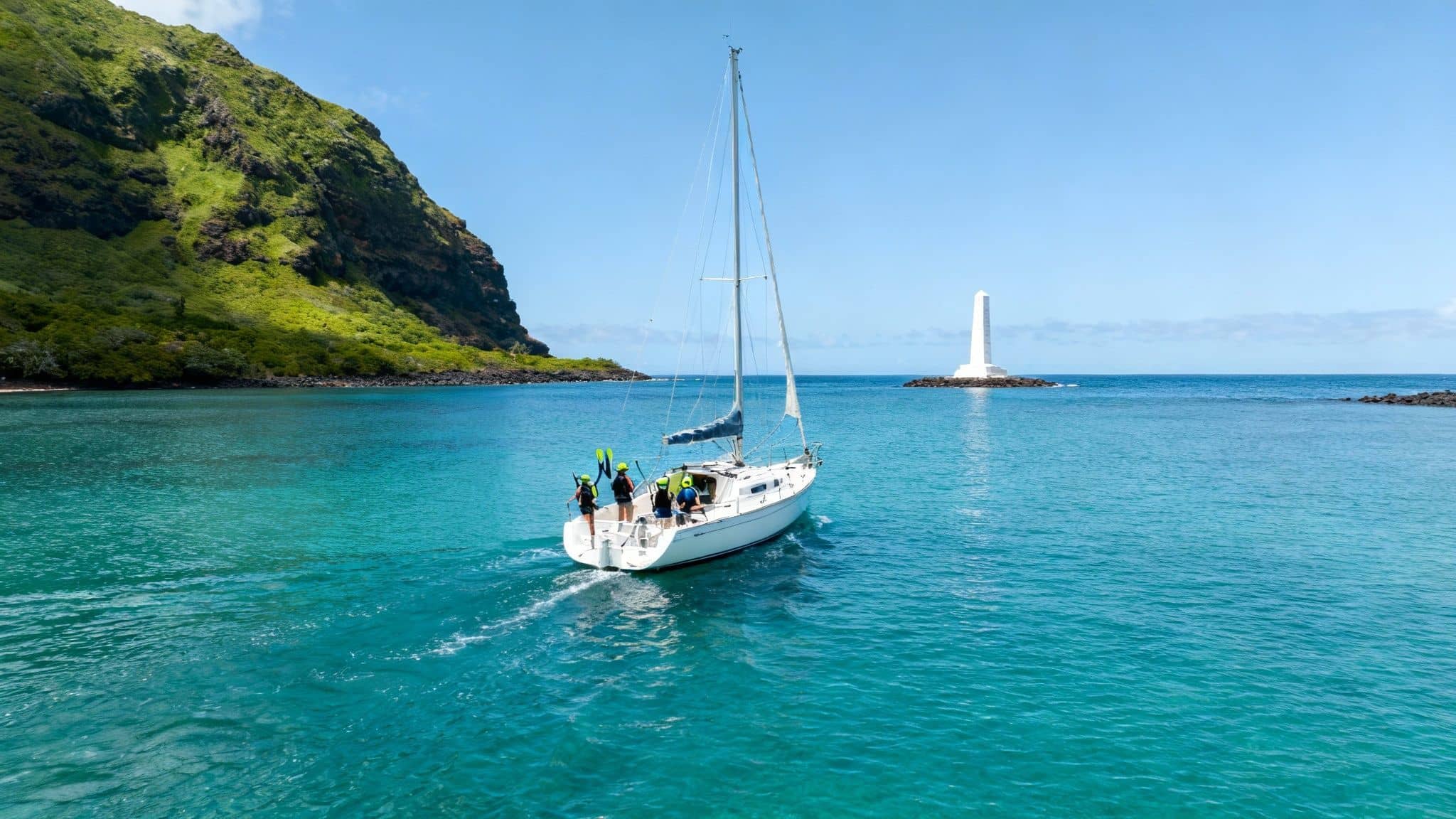 Sailboat floating on the calm, turquoise waters of Kealakekua Bay near lush green cliffs.