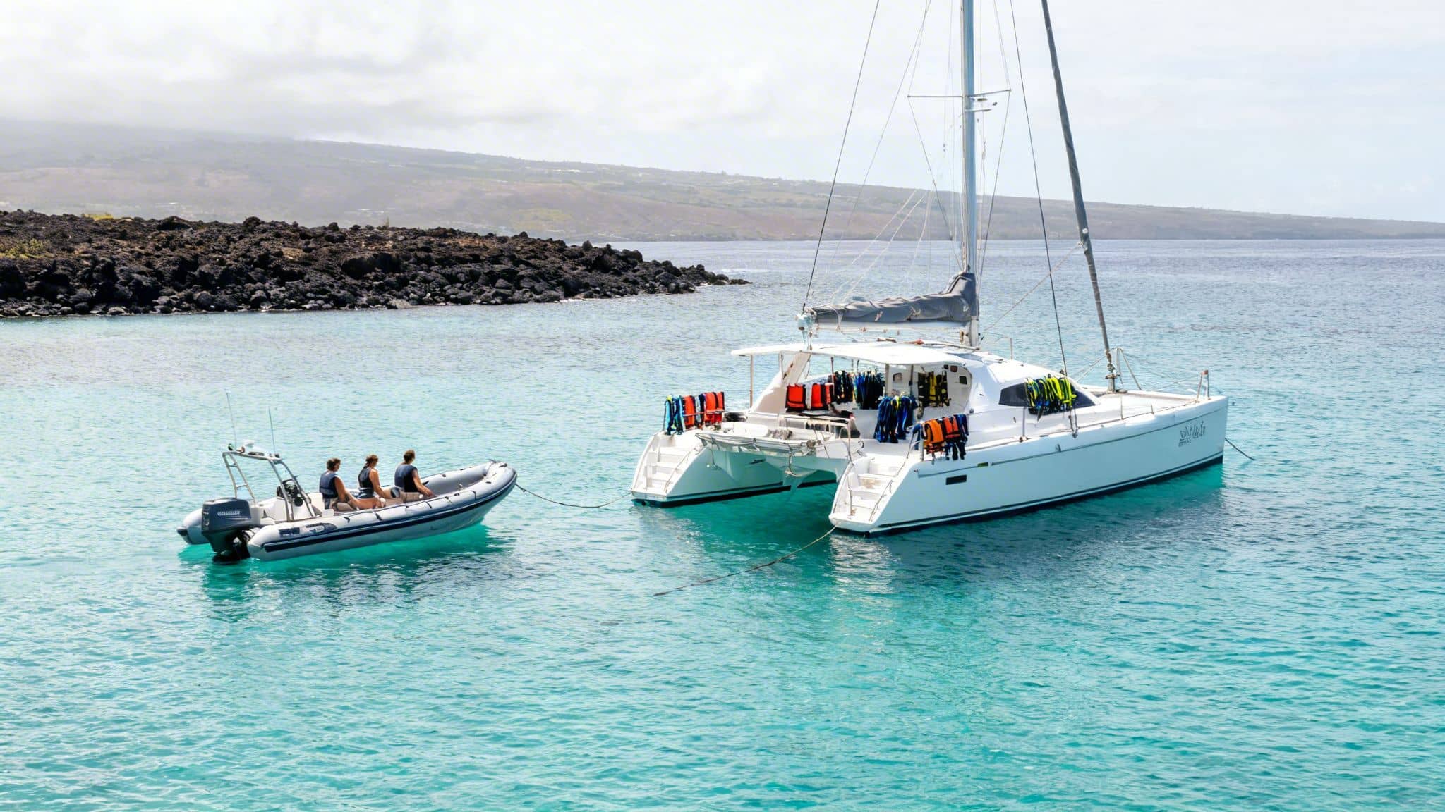 Catamaran and small boat with passengers and snorkel gear in clear tropical waters near island.