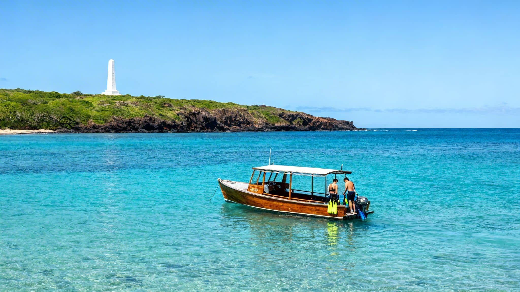 Tour boat with snorkelers in turquoise water near a tropical island and monument.