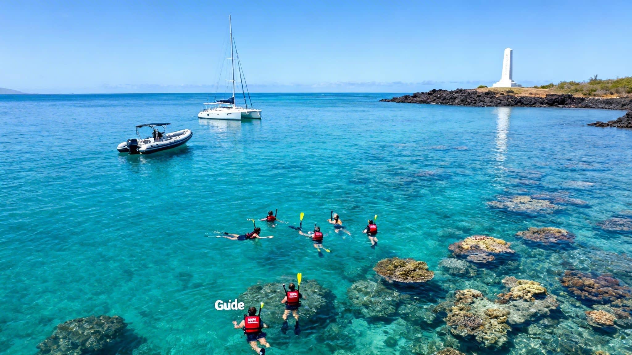 Aerial view of snorkelers exploring vibrant coral reefs in turquoise ocean water with boats and a monument.
