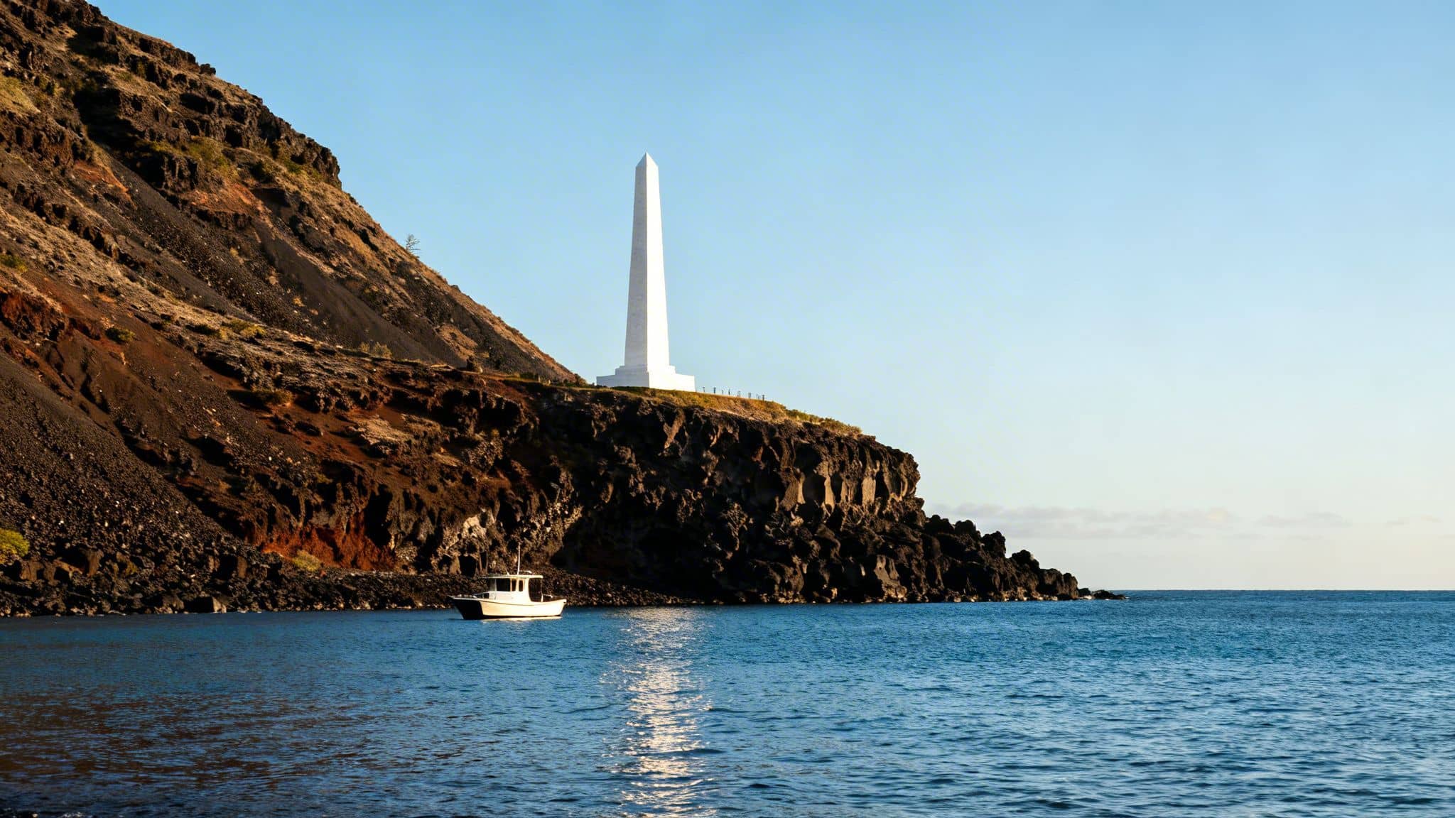 White obelisk on a dark volcanic cliff overlooking blue ocean with a small boat.