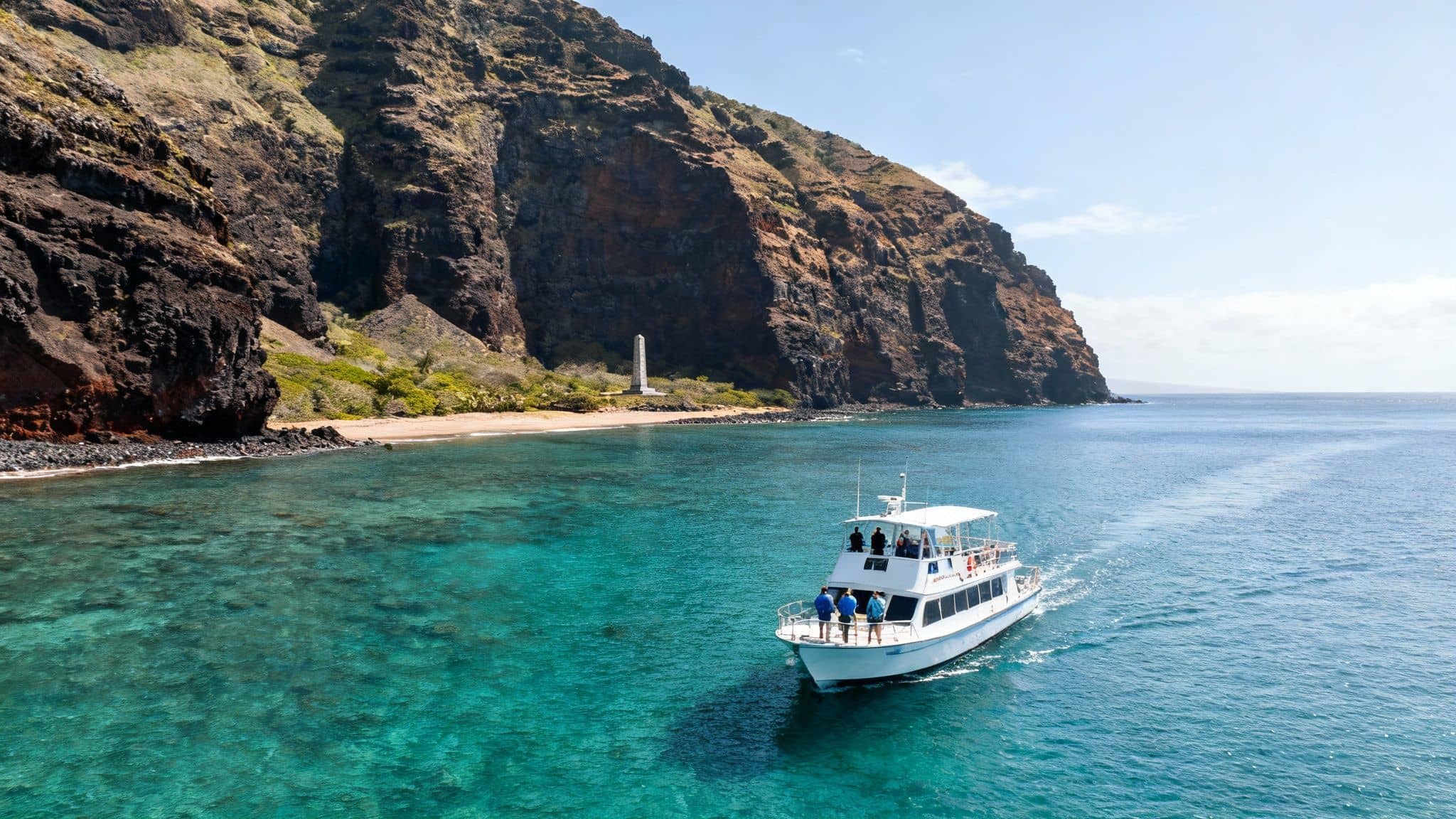 A white tour boat with passengers sails on clear turquoise water near a rocky coast and a monument.