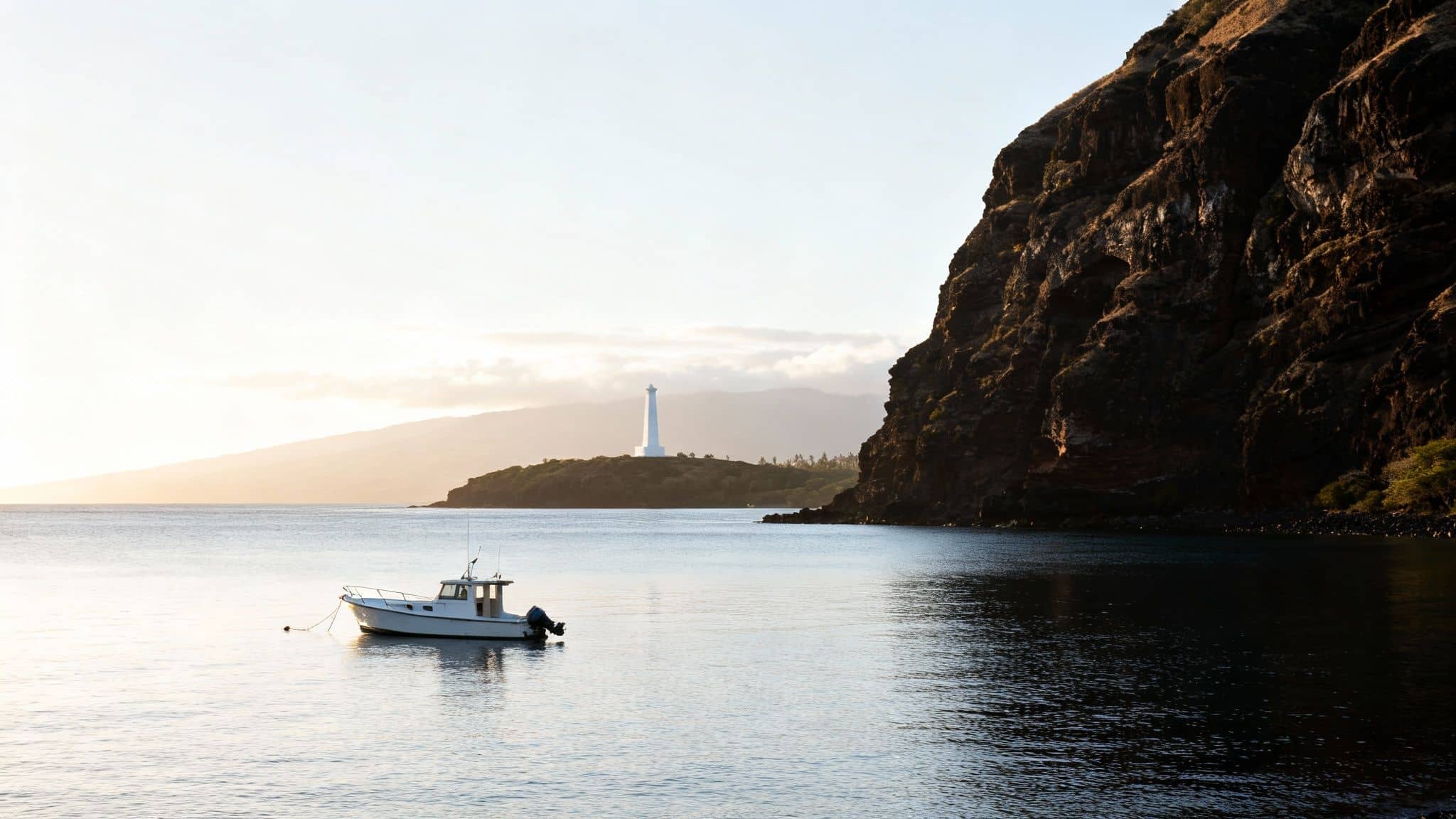 A white boat anchored in calm water with a lighthouse on a distant shore and a dark cliff.