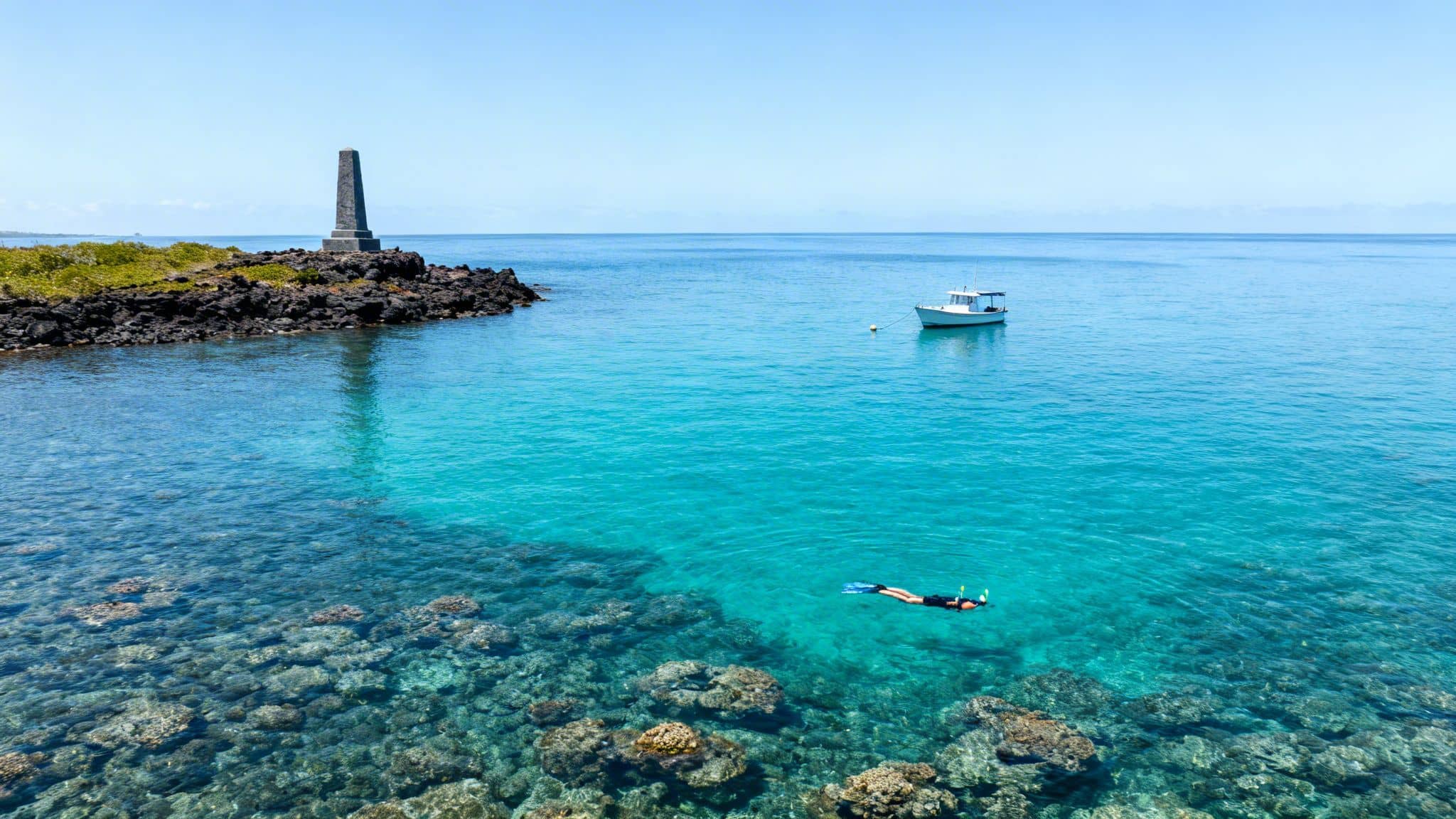 A person snorkels over a vibrant coral reef in clear turquoise water near a monument.