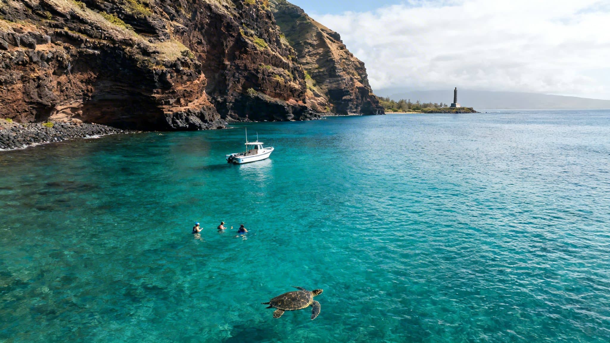 Aerial view of a sea turtle swimming near snorkelers and a boat in clear turquoise ocean water.
