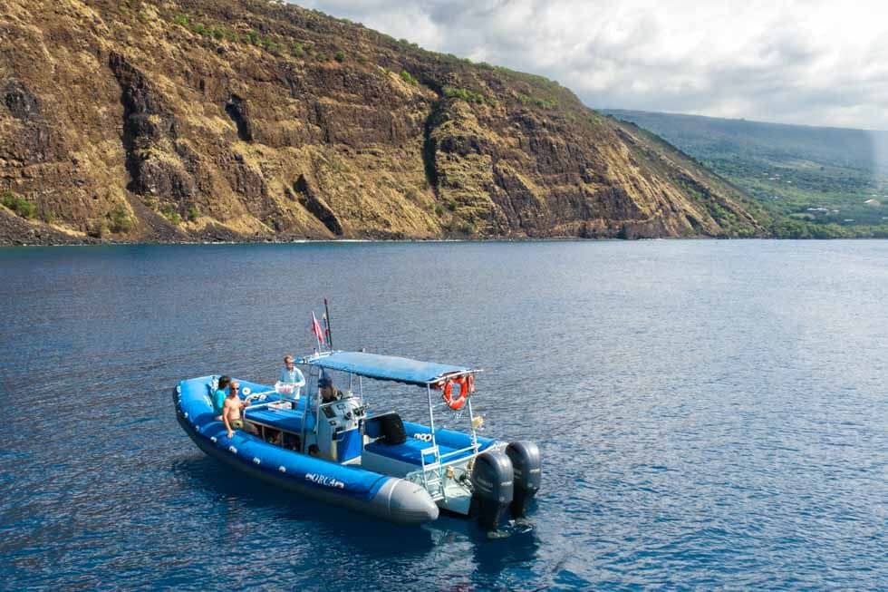 The blue Captain Cook RHIB boat idling beneath the Kealakekua Bay cliffs